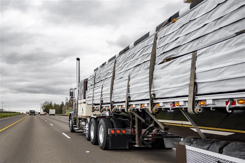 Classic Peterbilt with flatbed hauling wrapped materials on highway