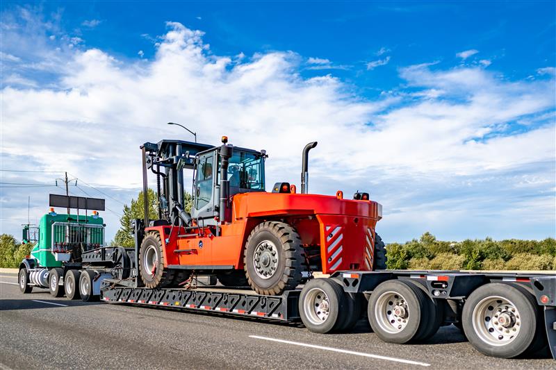 Green semi truck hauling red industrial loader on lowboy trailer