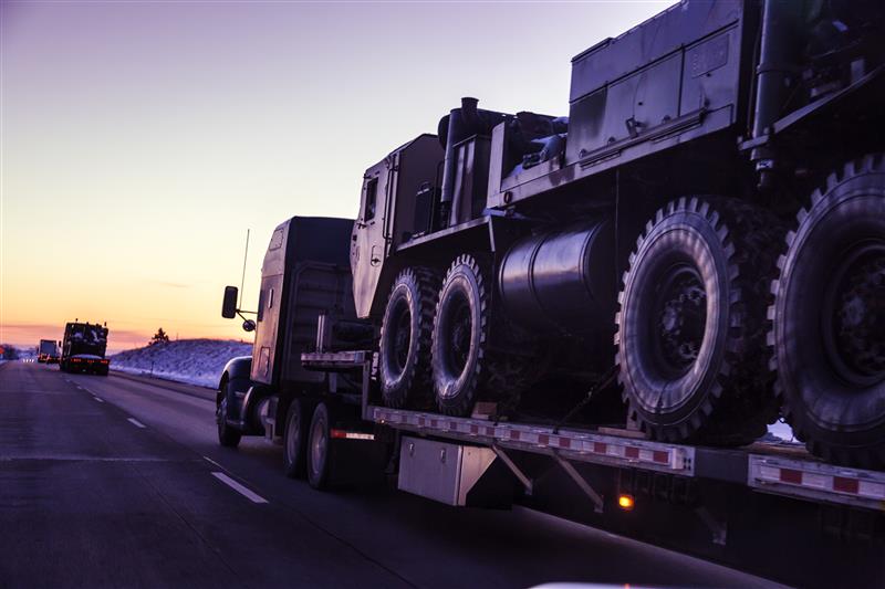 Heavy haul convoy transporting military vehicles at dusk on highway