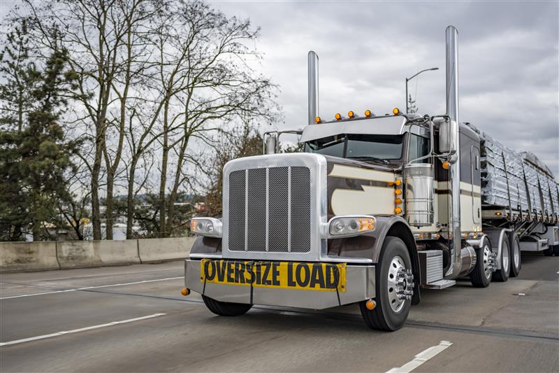 Silver Peterbilt truck with OVERSIZE LOAD banner hauling materials on highway